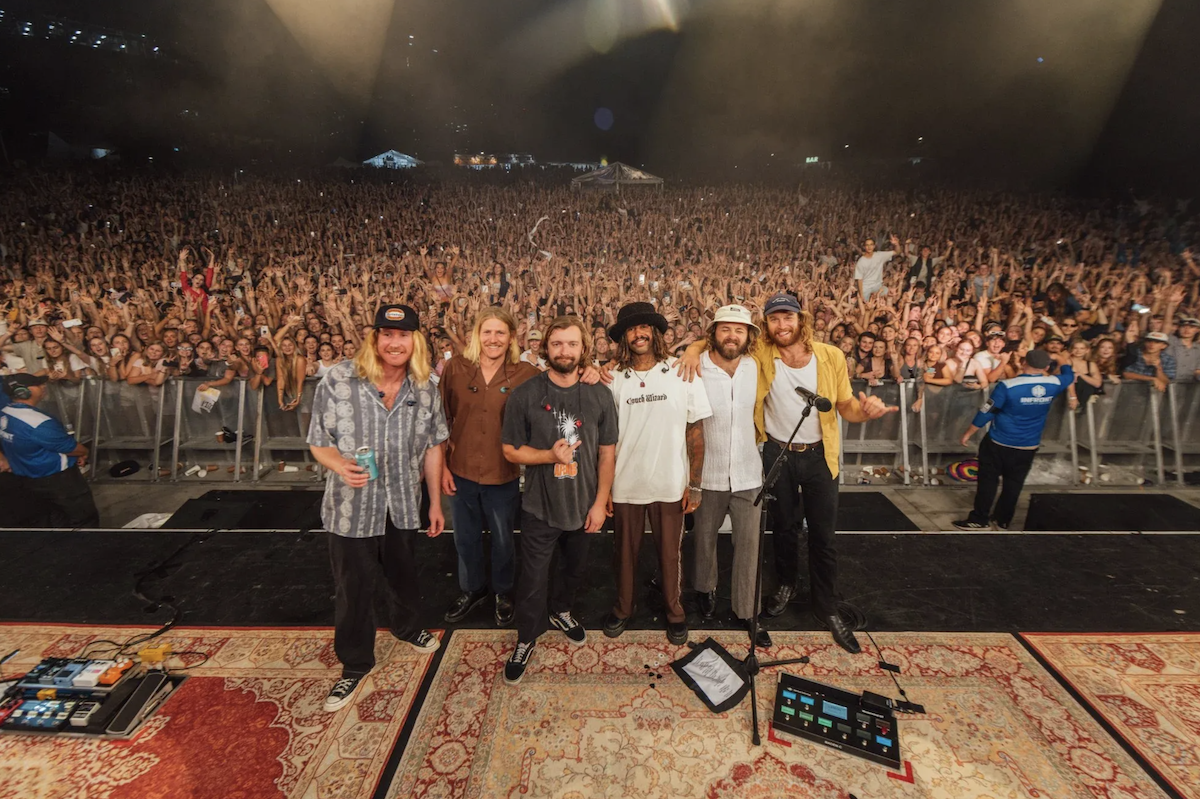 Australian rock band Ocean Alley posing on stage together in front of a massive cheering festival crowd after a live concert.
